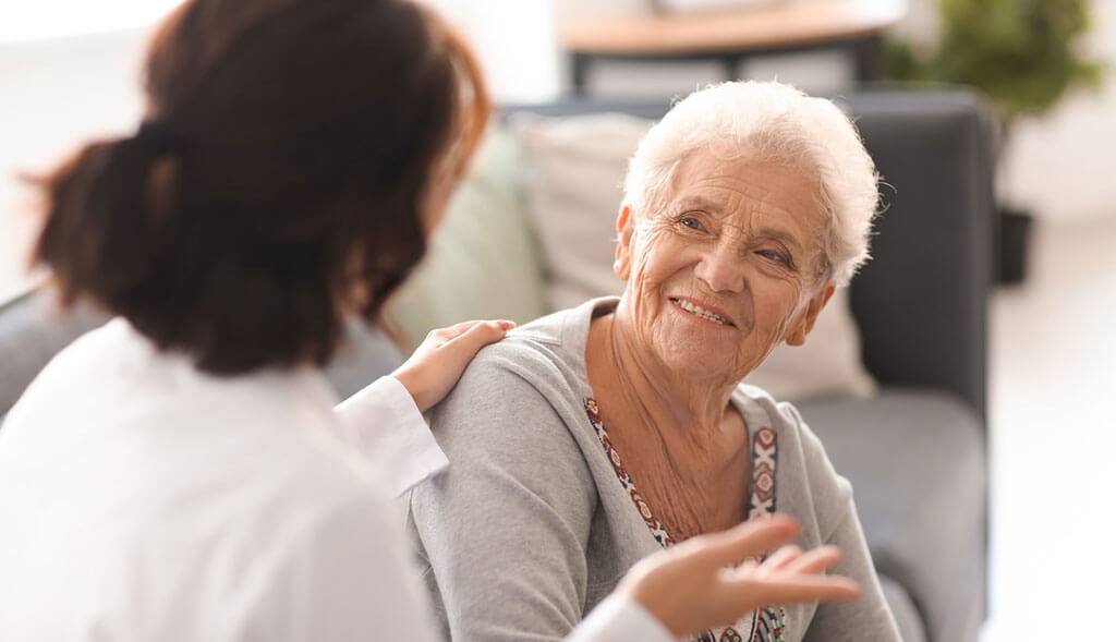 Home health aide talks with elderly woman.