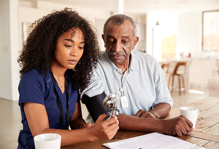 Home healthcare worker takes elderly man's blood pressure.